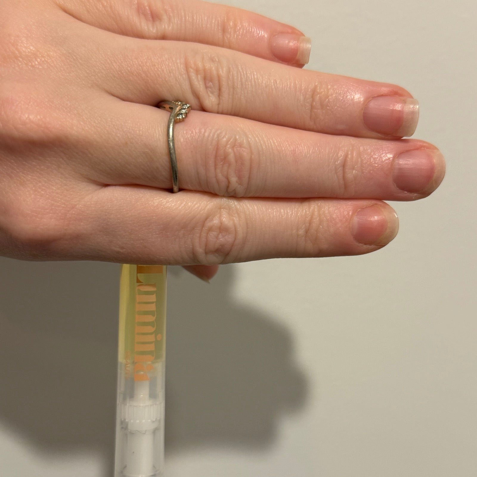 A hand resting beside the Lumina Beauty nail oil pen